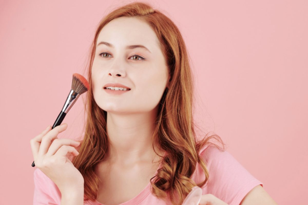Donna dai capelli rossi che applica blush con pennello