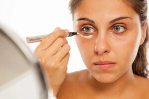 Donna allo specchio che copre occhiaie con correttore